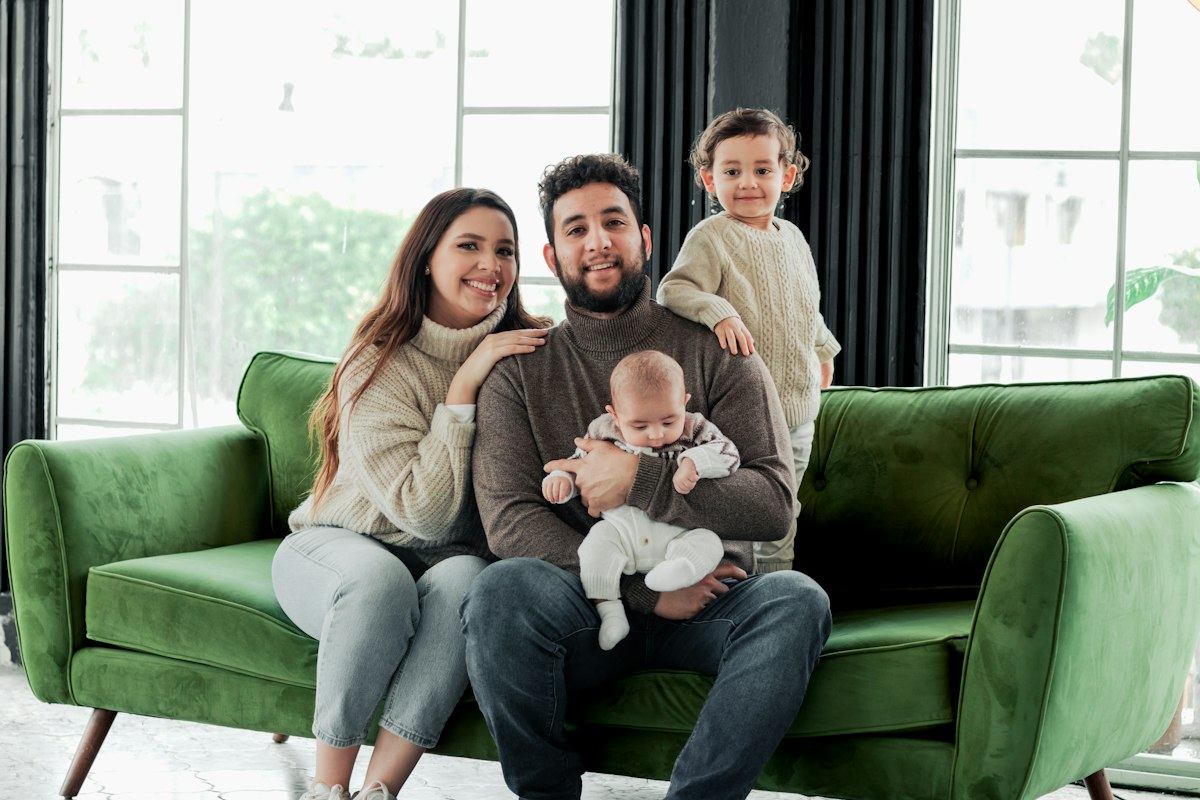A smiling family with a baby and a toddler sitting together on a green couch at home